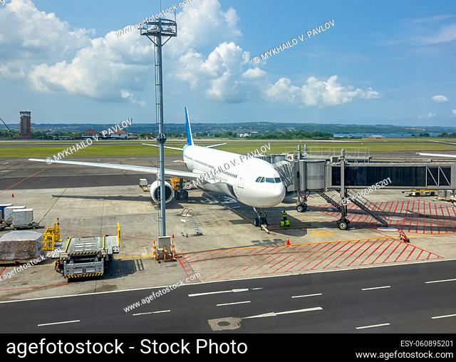 Sunny day at the Indonesian airport. An aircraft with an attached jet bridge for boarding and disembarking passengers. Ocean and jungle in the background