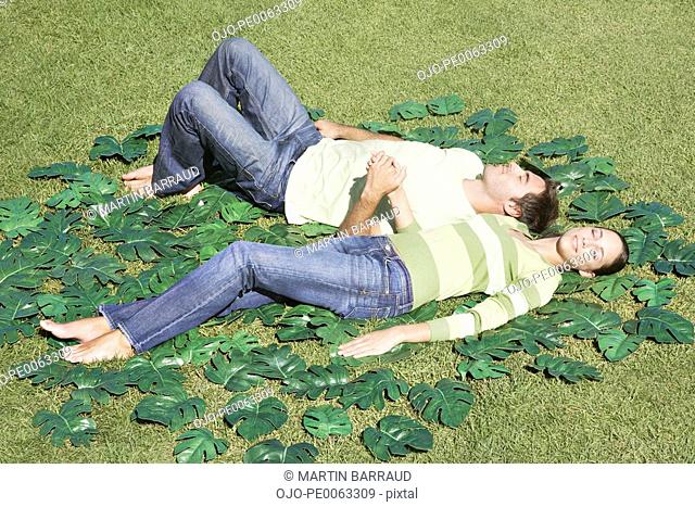 Couple laying in grass surrounded by green leaves