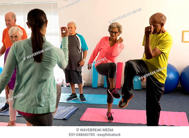 Rear view of female trainer assisting senior people in fitness studio