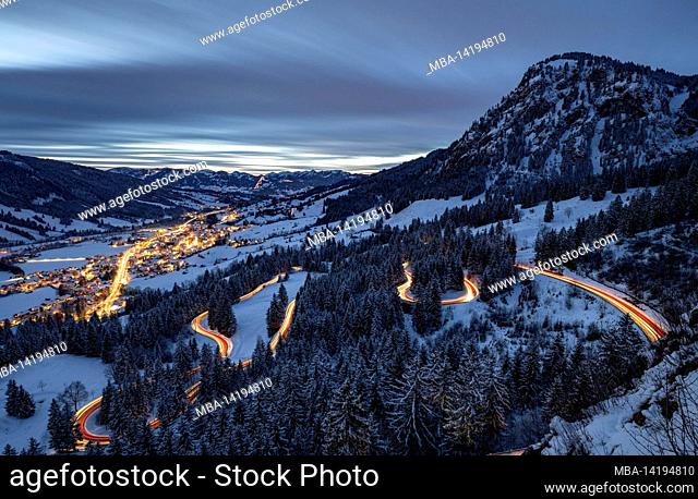 Bad Hindelang and Jochpassstrasse illuminated in the evening in a snowy winter landscape. Framed by the snow-capped Allgäu Alps