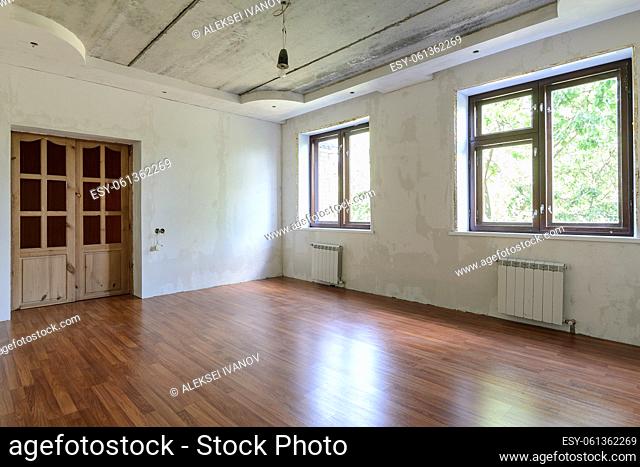 Interior of an empty room during renovation, view of a wall with windows and a wall with a door