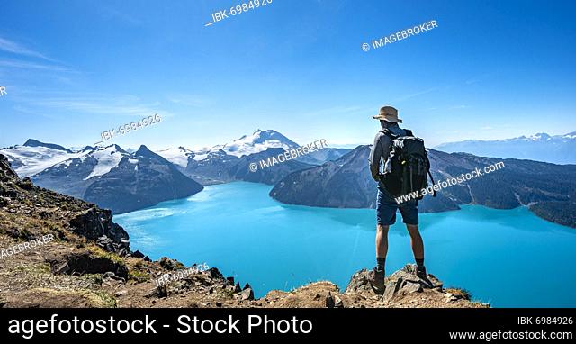 Young man looking into the distance, view of mountains and glacier with lake Garibaldi Lake, summit Panorama Ridge, Guard Mountain and Deception Peak