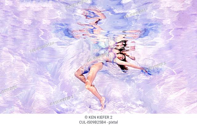 Underwater view of woman draped in sheer fabric, floating towards water surface