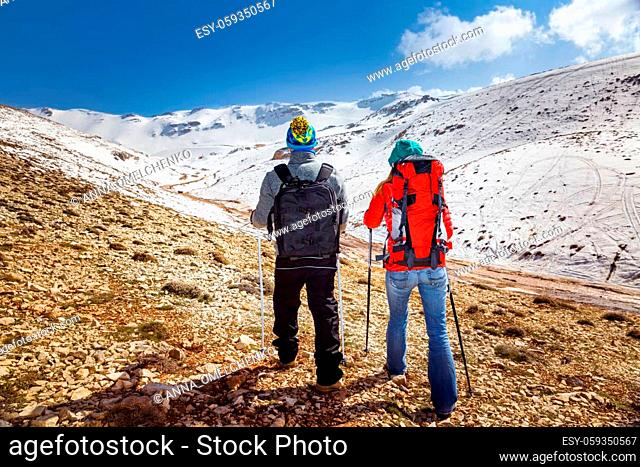 Back Side of a Young Family Hiking in the Mountains with Trekking Poles. Enjoying Amazing View on Beautiful Snowy Mountains