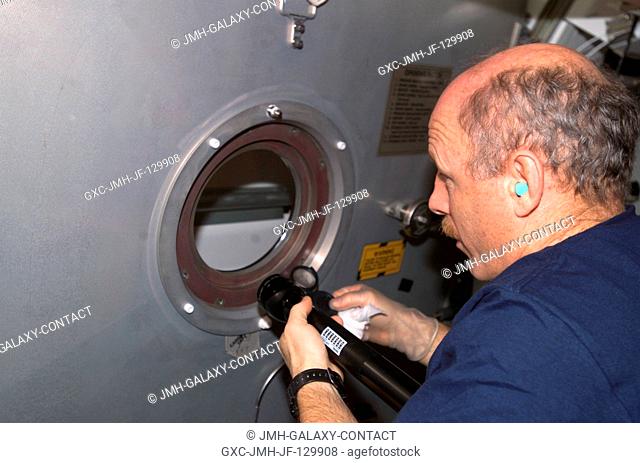 Astronaut Kenneth D. Bowersox, Expedition Six mission commander, holds a flashlight as he looks through a portal in the Zvezda Service Module on the...