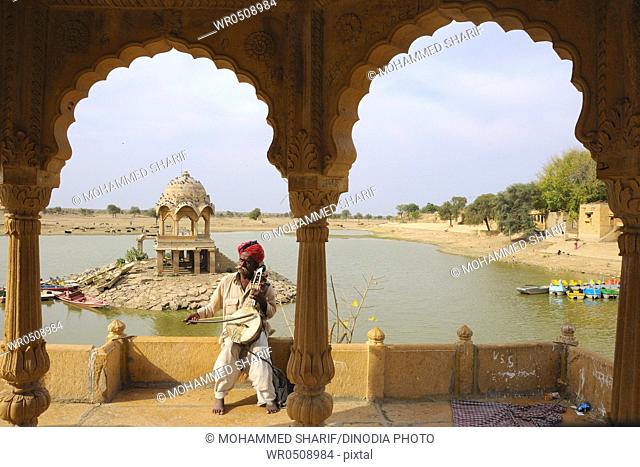 Folk musician playing musical instrument at Gadsisar Gadisar lake , Jaisalmer , Rajasthan , India MR772B