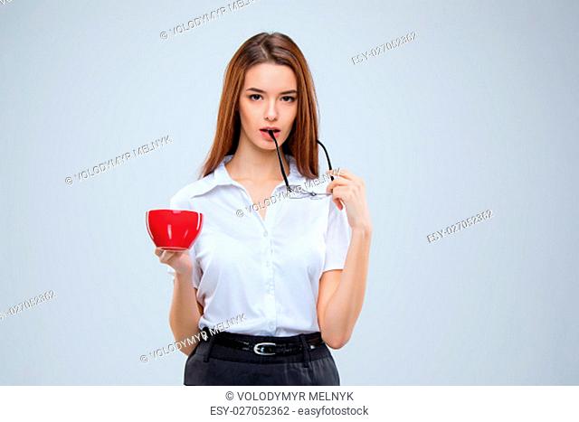 The young business woman in glasses with red cup of coffee on a gray background