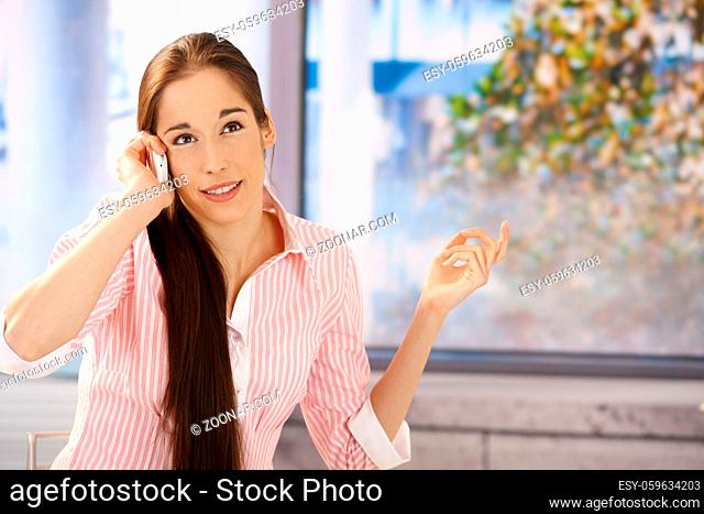 Smiling girl concentrating on phone conversation in front of window