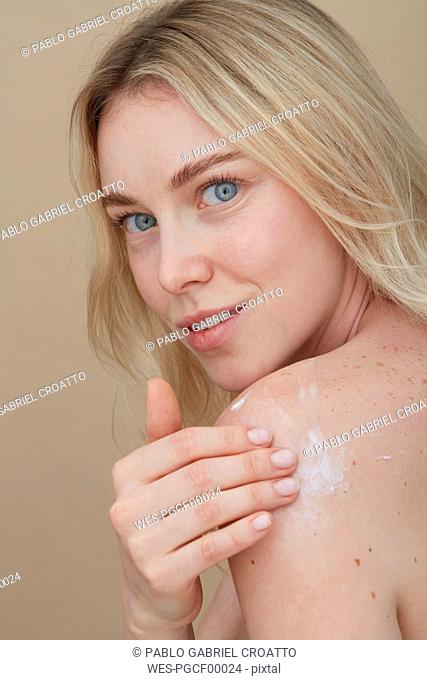 Portrait of blond young woman applying cream on her shoulder