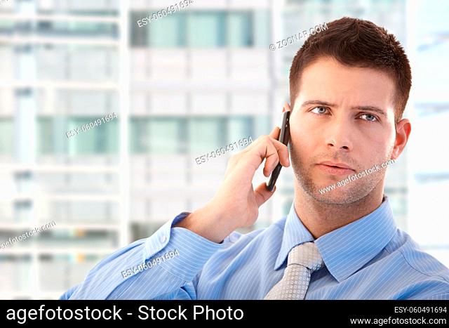 Handsome young businessman using mobile phone in modern office front of window