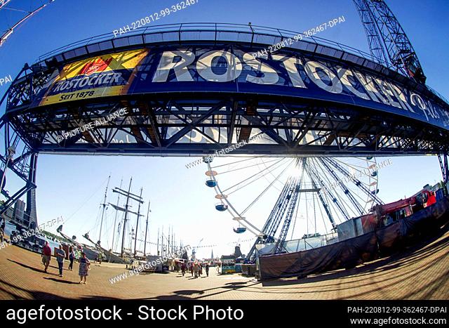 12 August 2022, Mecklenburg-Western Pomerania, Rostock/Warnemünde: View of the gantry crane, a Ferris wheel and sailing ships in Rostock's city harbor for the...