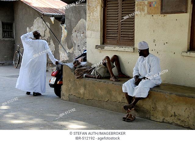 Local men dressed in white capes rest in an alley in Stone Town Zanzibar Tanzania