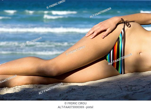 Woman in bikini lying on beach, low section