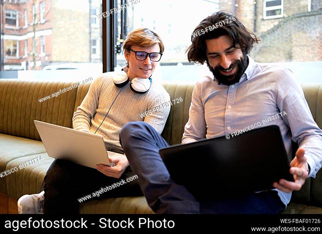 Businessmen with laptop discussing while sitting on sofa in office