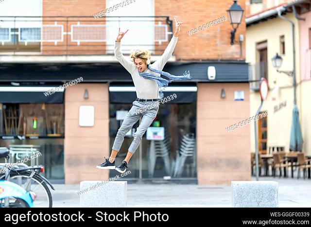 Carefree young man jumping from bench with hands raised in city