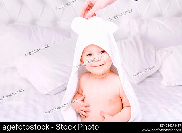 Adorable newborn baby boy with brown eyes sitting wrapped in a white towel with ears in light bed. A happy childhood and the concept of health
