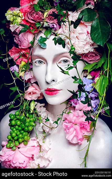 Beautiful young pale white woman with different flowers on head. Flower queen. Beauty shot on black background