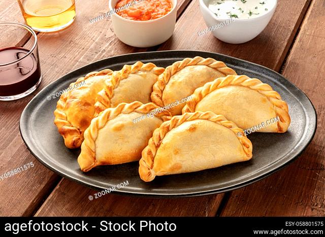 A closeup of Argentinian empanadas with sauces and wine on a dark rustic wooden background