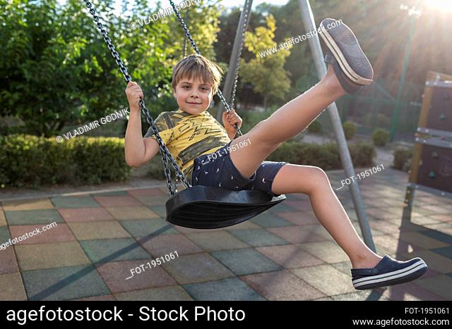 Portrait carefree boy swinging at sunny park playground
