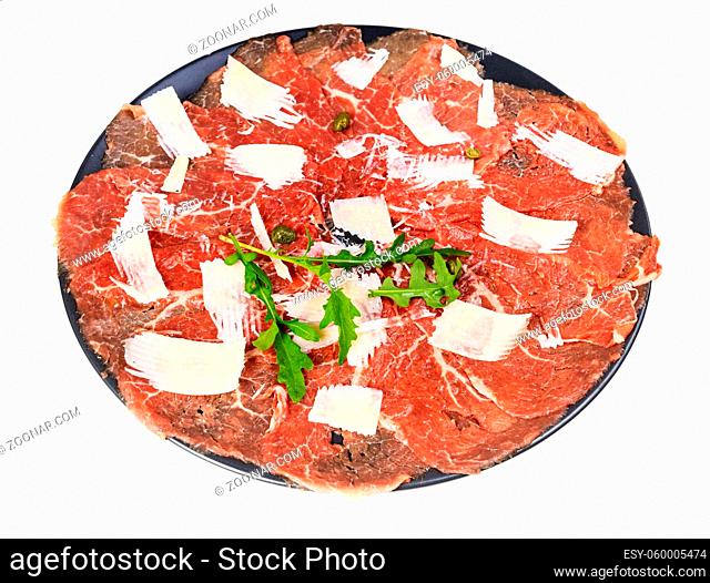 portion of Carpaccio (thinly sliced raw beef fillet) decorated by Parmesan, Arugula and capers on black plate isolated on white background