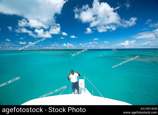 Crew member standing and gesturing in the bow of a resort's tourist boat; Republic of the Maldives