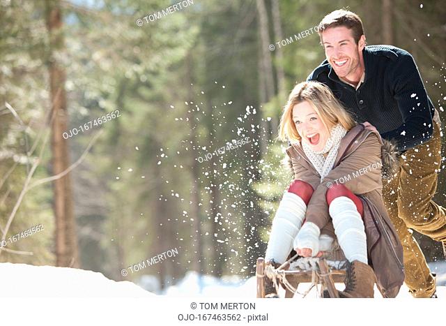 Man pushing woman on sled in snowy woods