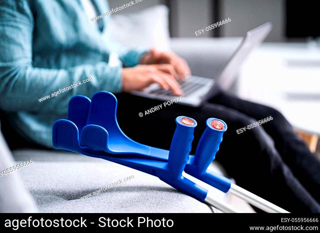 Injured Man With Broken Leg And Crutches Using Laptop