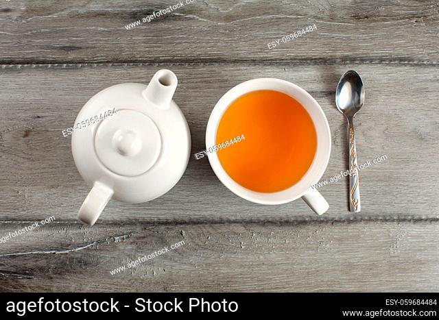 Table top view on white ceramic teapot, cup of hot black tea, and silver spoon placed on gray wood desk