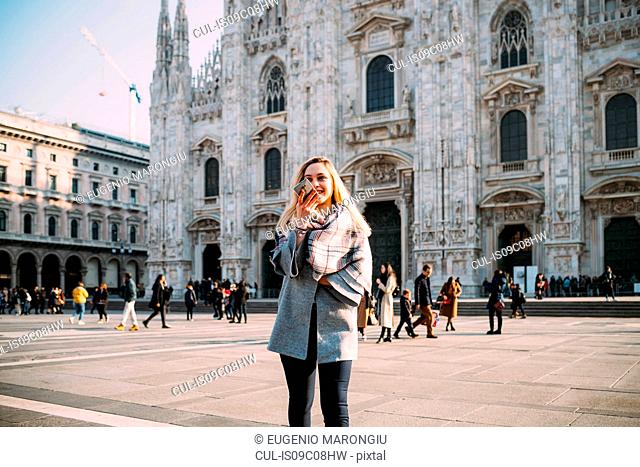 Young female tourist talking at smartphone by Milan Cathedral, Milan, Italy