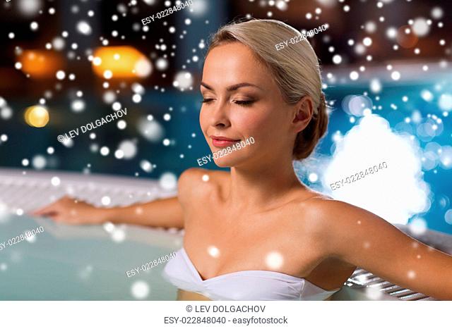 people, beauty, spa, healthy lifestyle and relaxation concept - beautiful young woman wearing bikini swimsuit sitting in jacuzzi at poolside with snow effect