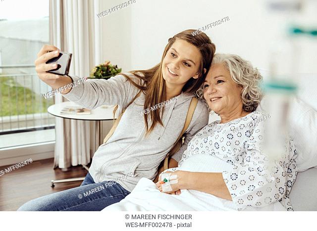 Granddaughter visiting grandmother in hospital, taking selfie with smart phone