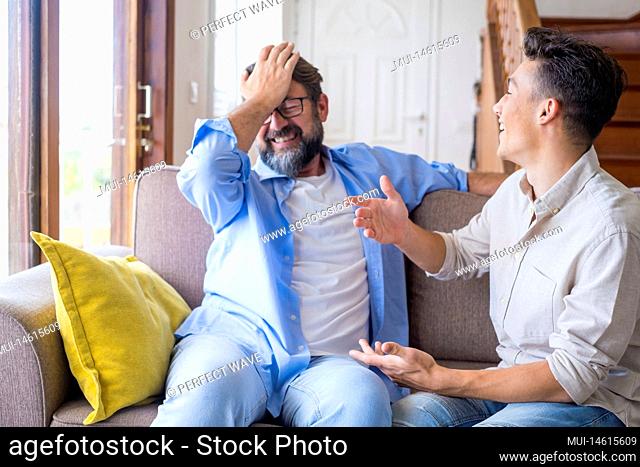 Happy father and son chatting on sofa at home. Cheerful father with teenage son sitting on couch in the living room of apartment