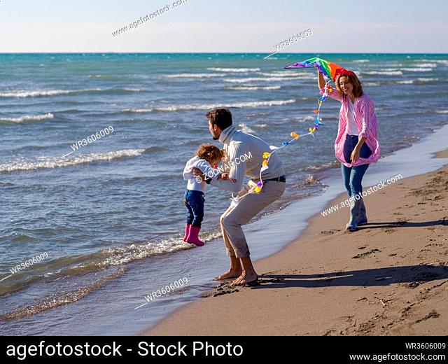 Family with little daughter resting and having fun with a kite at beach during autumn day