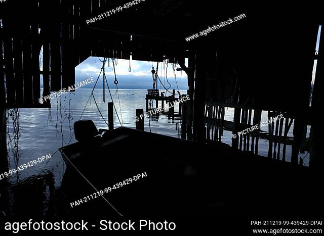 19 December 2021, Bavaria, Utting: A boat lies shortly before sunrise in a partly dilapidated boathouse at the Ammersee. Photo: Karl-Josef Hildenbrand/dpa