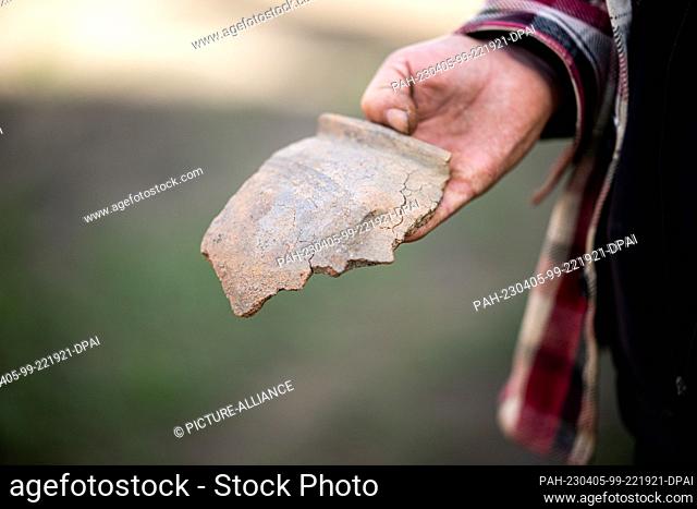 05 April 2023, Schleswig-Holstein, Lohe-Rickelshof: A man holds a piece of a ceramic pot estimated to date from the 1-2 century AD