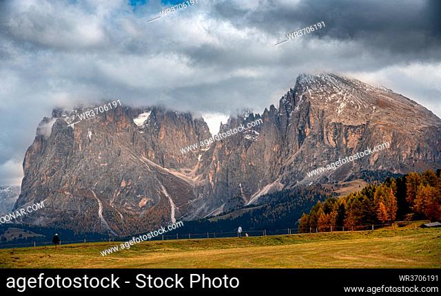 Beautiful mountain landscape with Dolomite rocky peak covered with clouds and unrecognised people hiking at the at the famous Alpe di Siusi valley South Tyrol...