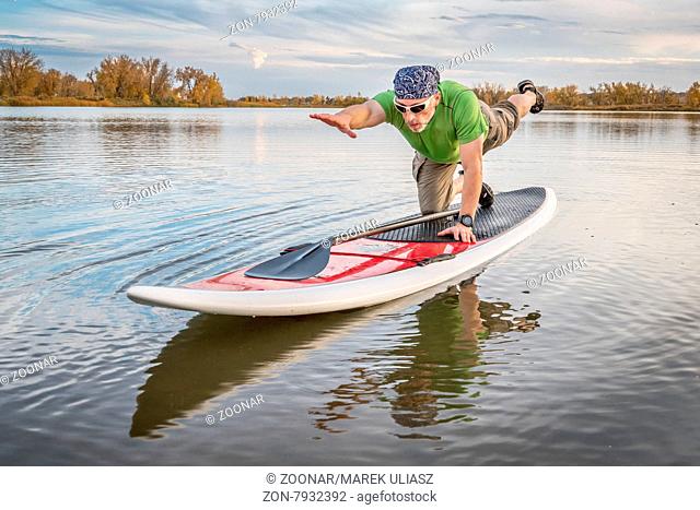 senior male stretching and warming up on a paddleboard before paddling workout on a lake in Colorado