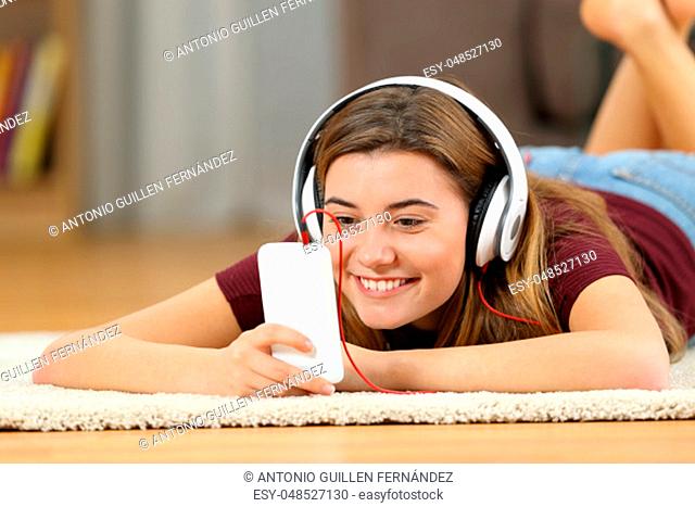 Happy teen watching media content on line in a smartphone lying on a carpet on the floor of the living room at home