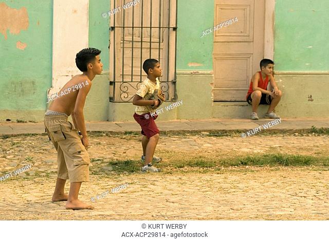 A group of teenage boys playing a game of baseball in the streets of Trinidad Cuba