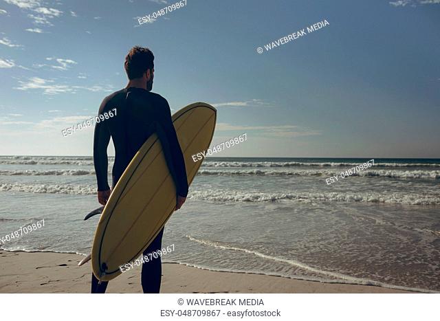 Male surfer with a surfboard standing on a beach