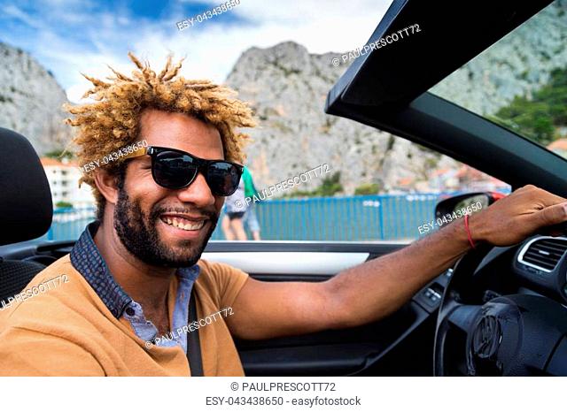 Young happy black man with dread locks wearing sunglasses sitting in the convertible car