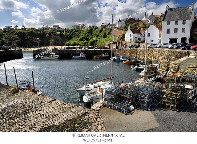 Stone pier walls at Crail Harbour with fishing boats and lobster traps and cliff with beach at Crail Fife Scotland UK