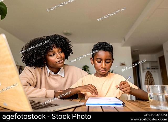 Smiling young woman with son studying at home