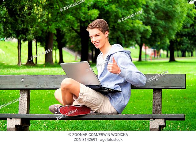 Ein Teenager mit Laptop im Freien. Sitzt im Park. Mobiles Internet