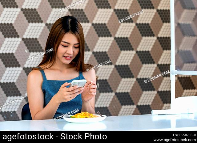 Portrait of asian influencer food blogger or vlog take food photo at new normal social distance restaurant with table shiled partition