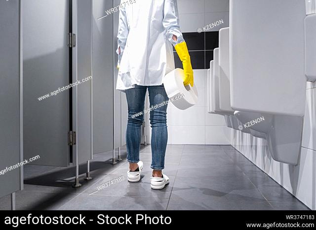 Janitor woman changing paper in public toilet or restroom
