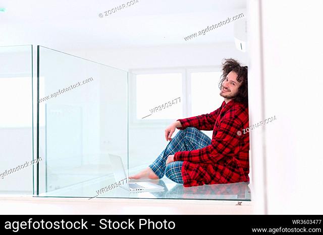 young freelancer in bathrobe working from home using laptop computer while sitting on floor