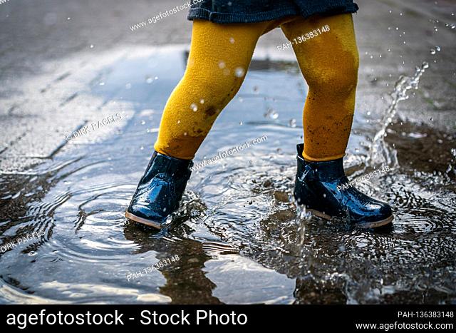 October 7th, 2020, Trebbin, a little girl with rubber shoes and yellow tights jumps around in a puddle and has a lot of fun. | usage worldwide