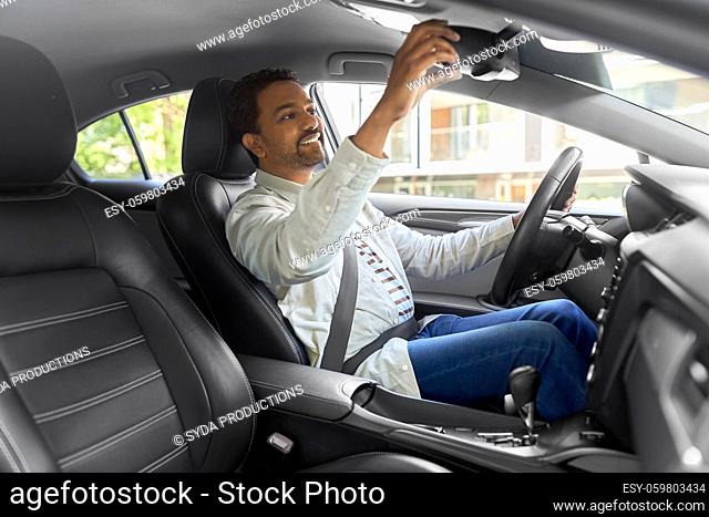 happy indian man or driver adjusting mirror in car