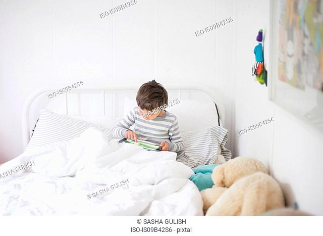 Boy sitting up in bed playing video game on digital tablet